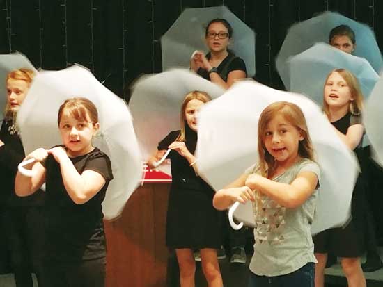 Photo of kids onstage with umbrellas.